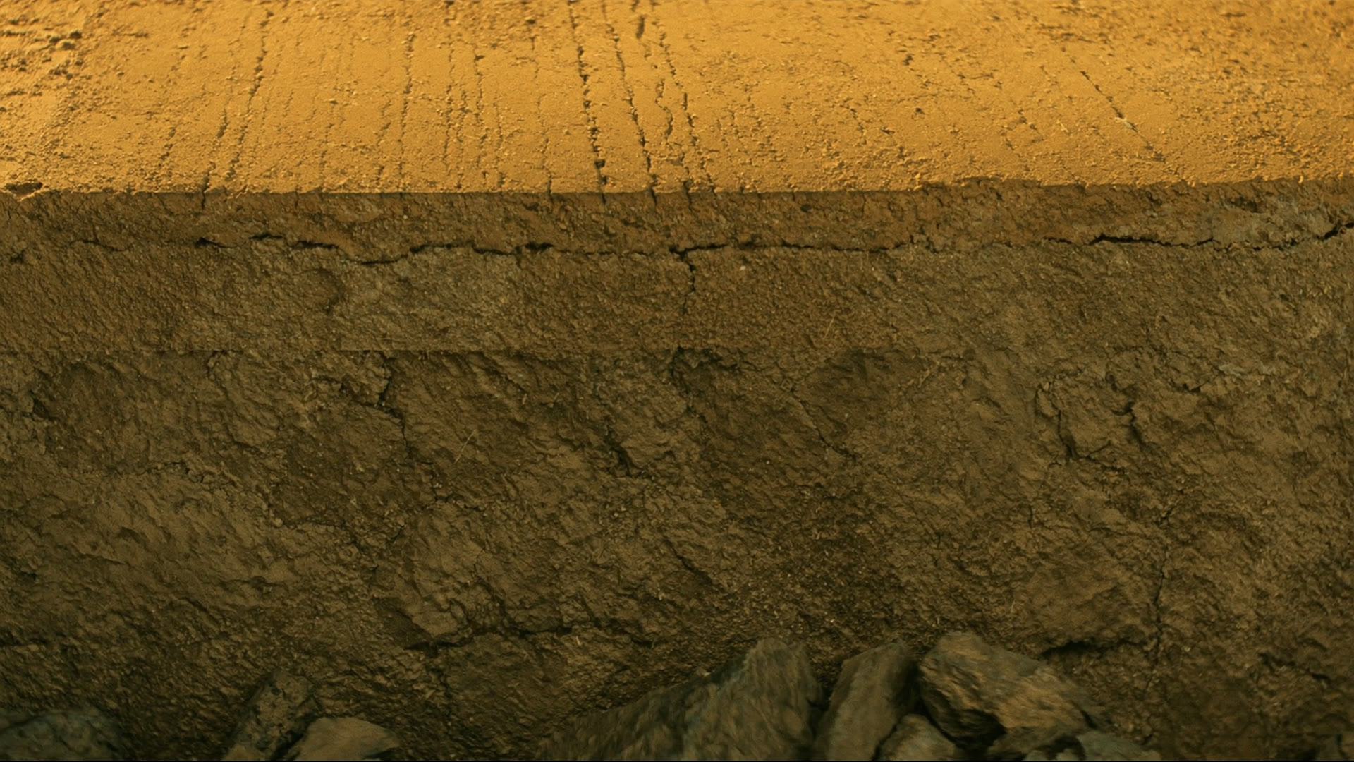 Kesilmiş basamak yüzünde makine izleri, üstte ochre toprak altta gri kaya